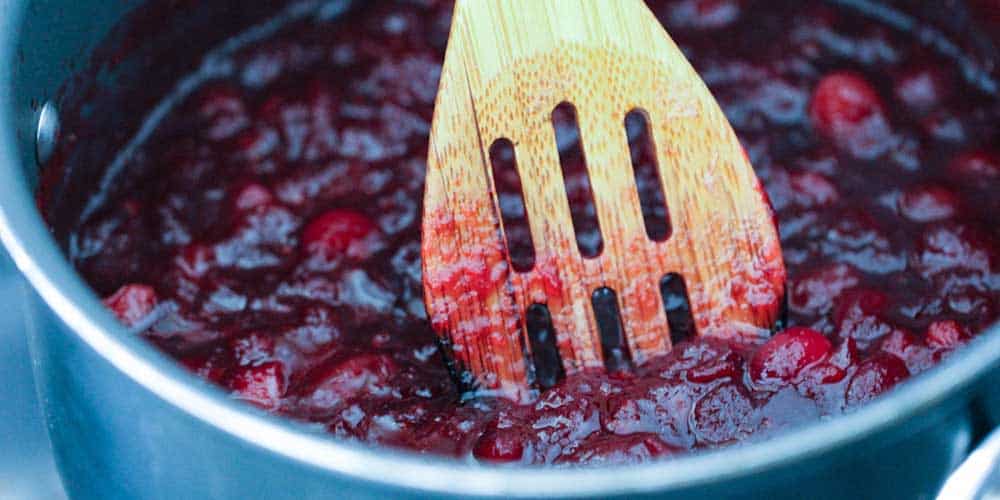 A wooden spoon in a pan of maple orange cranberry sauce. 