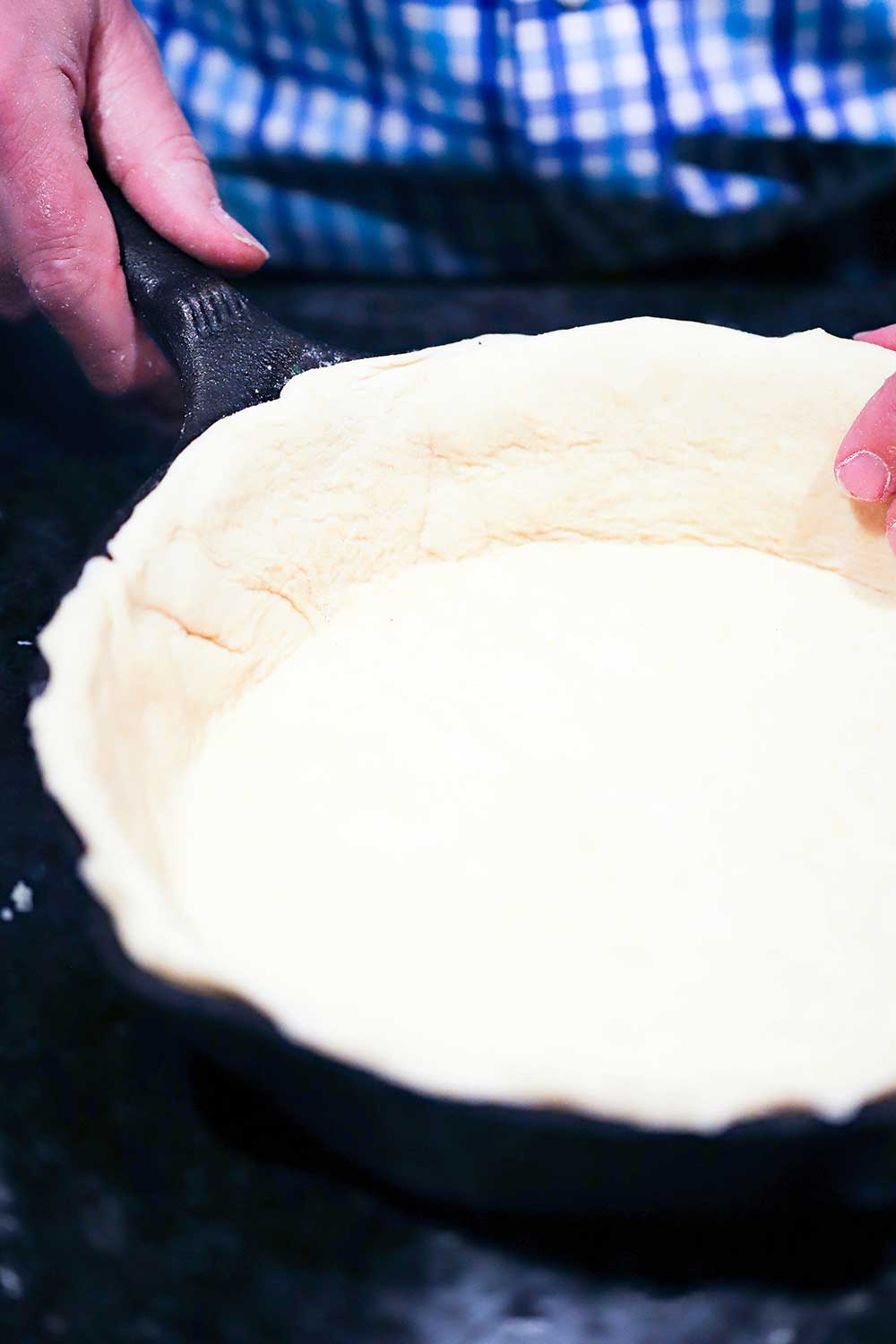 A person using his hands to press pizza dough into the inside of a cast-iron skillet. 