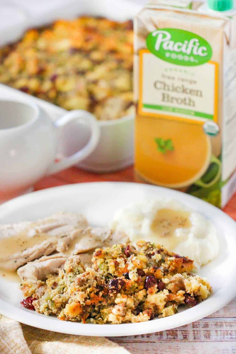 A plate full of roasted turkey, mashed potatoes and cornbread dressing with a box of broth next to it. 