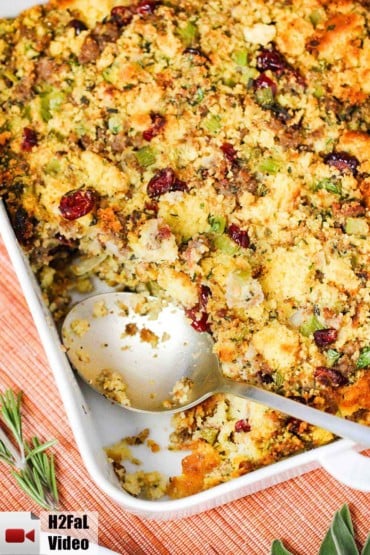 A square white dish holding cornbread dressing with sausage and cranberries