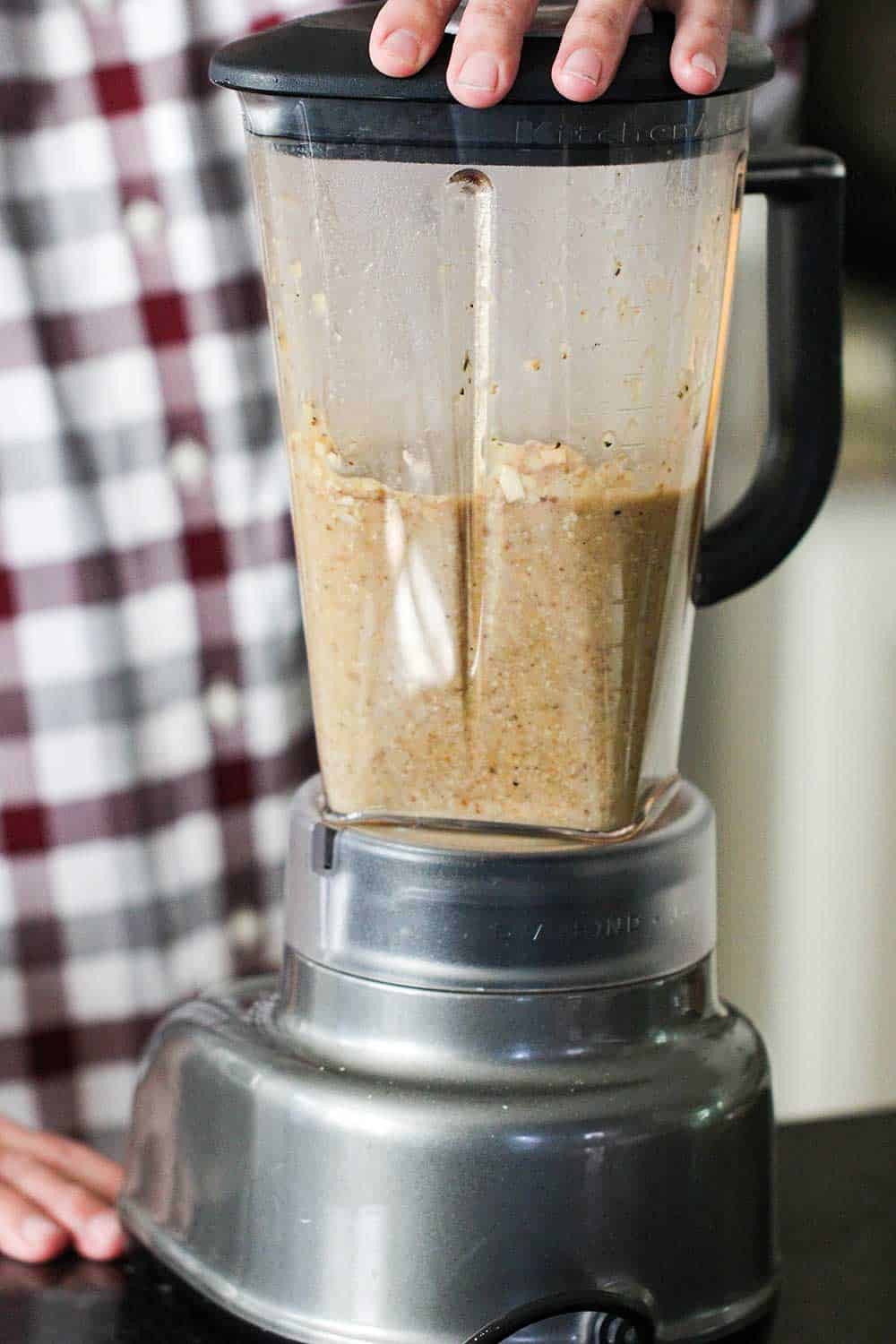 A blender of pureed mushroom soup with two hands holding it in place. 