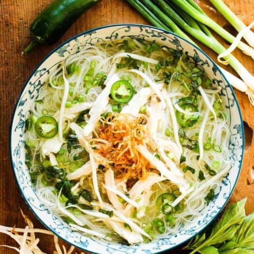 A bowl of pho and scallions and shallots on the side