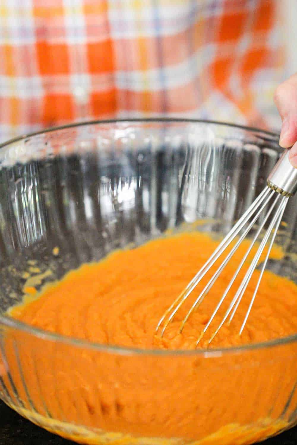 A large bowl filled with pumpkin puree, with a hand holding a whisk in the bowl. 