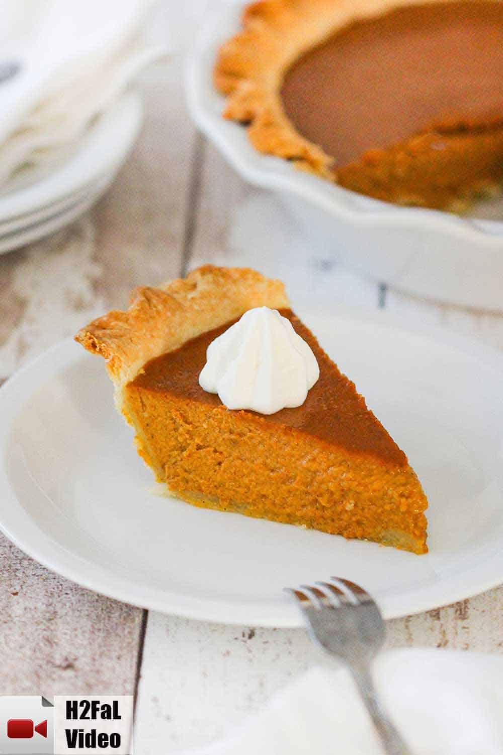 A slice of pumpkin pie on a white plate next to a whole pumpkin pie. 