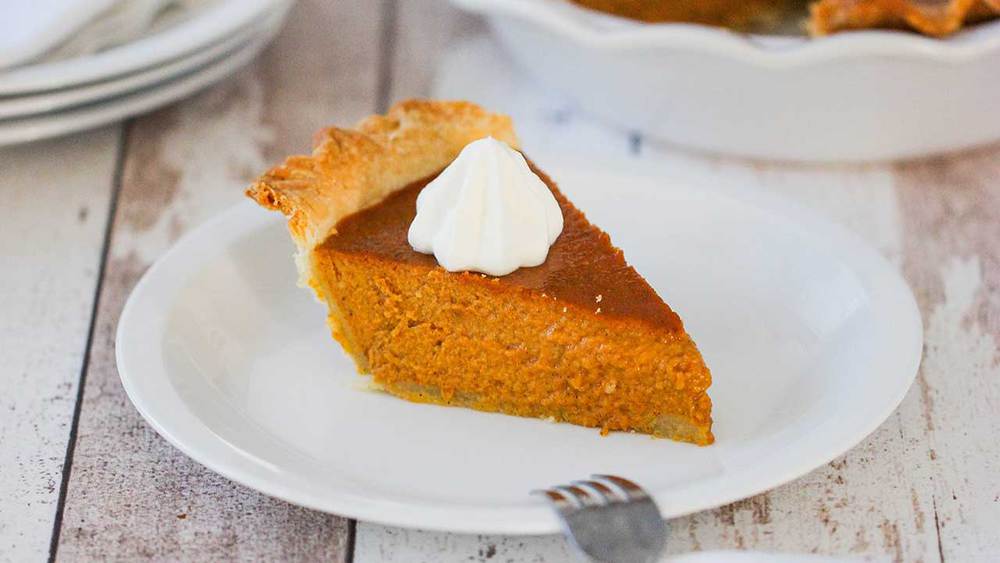 A slice of pumpkin pie with a dollop of whipped cream on top on a white dessert plate. 