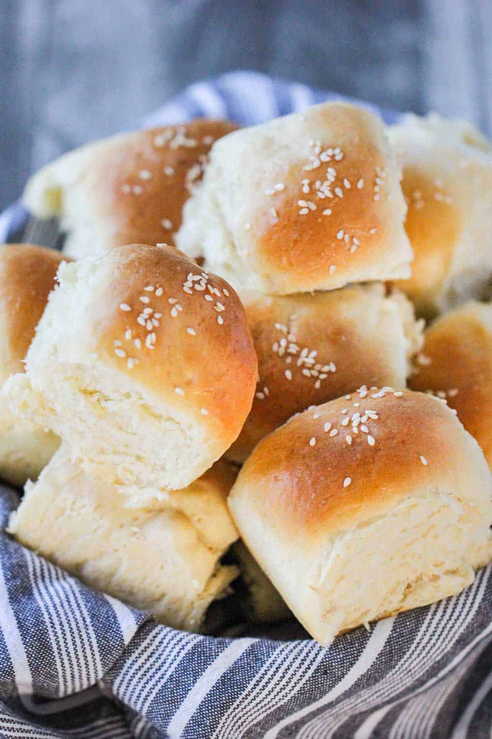 A basket lined with a grey cloth filled with homemade dinner rolls. 