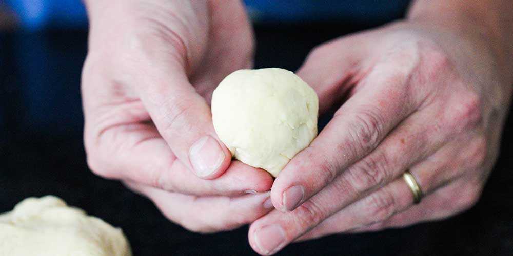 Two hands form a piece of dough for homemade dinner rolls. 
