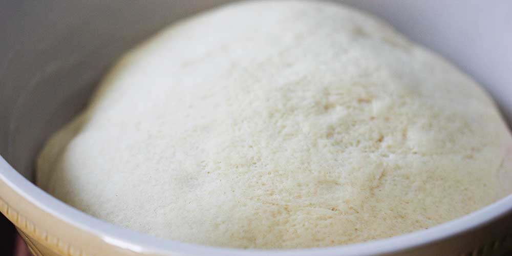 Dough for homemade dinner rolls that has doubled in size in a large ceramic bowl. 