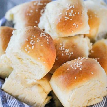 A basket lined with a grey cloth filled with homemade dinner rolls.