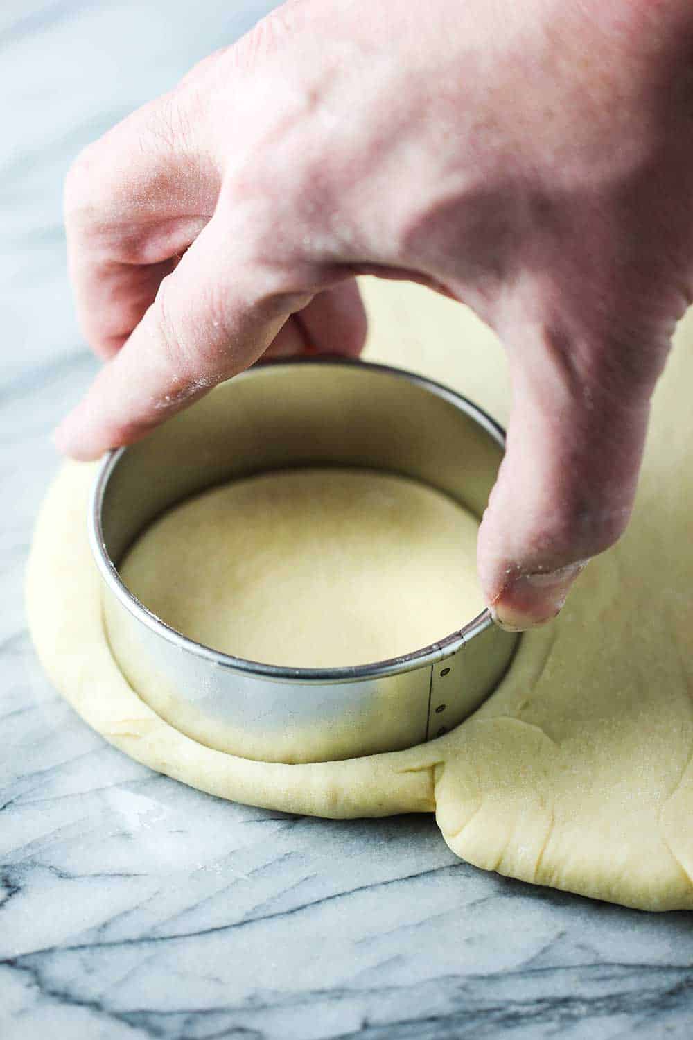 A hand using a cookie cutter to cut out a round from a layer of doughnut dough. 