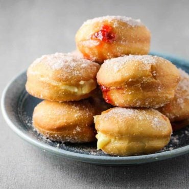 Jelly and custard doughnuts stacked on top of each other on a blue pattern plate.