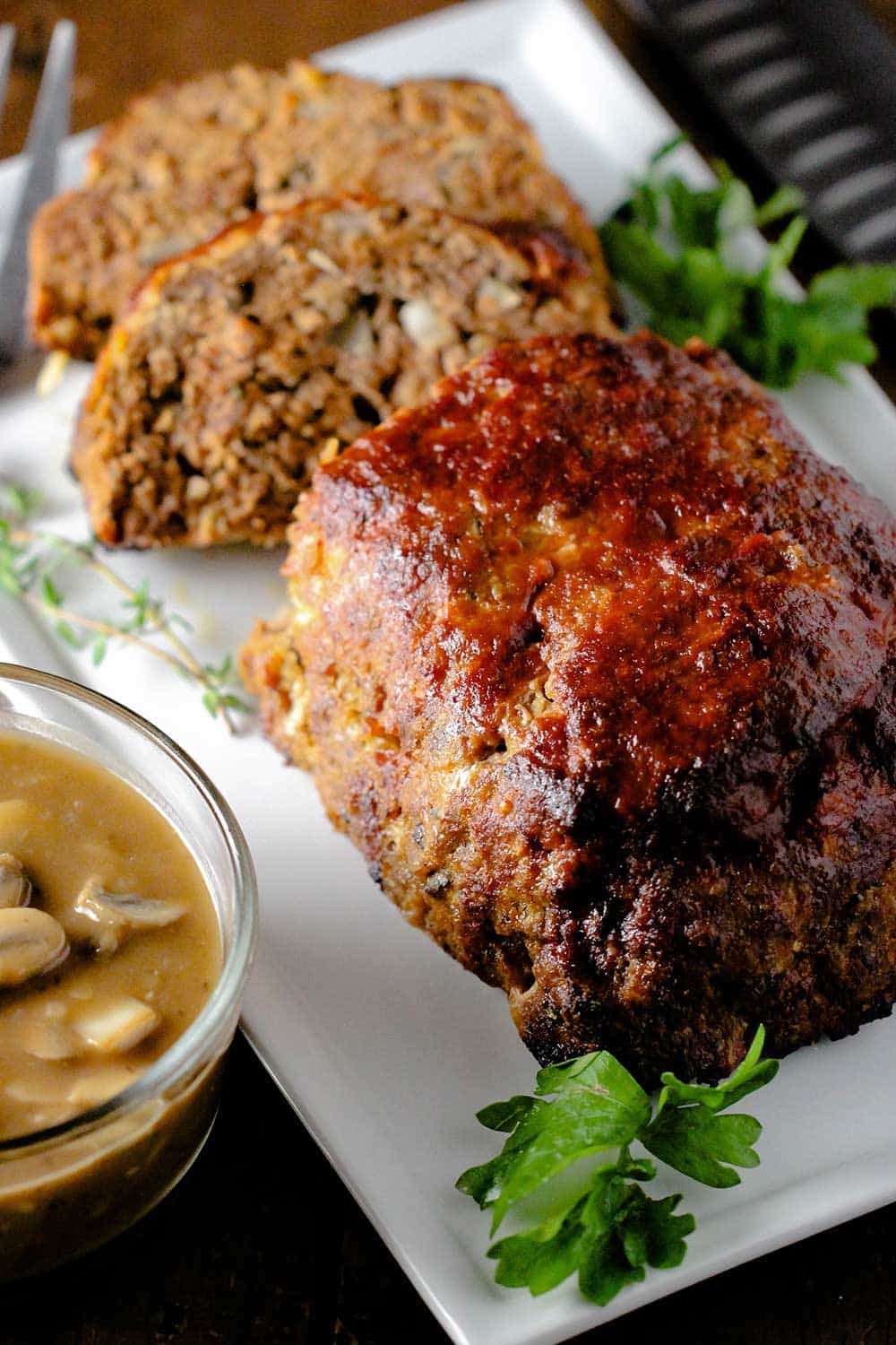 A best-ever meatloaf on a white platter next to a bowl of mushroom gravy. 