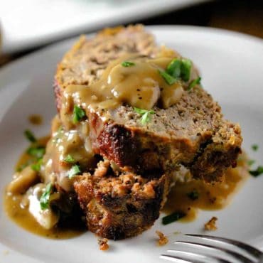 Two slices of meatloaf on a white plate with mushroom gravy poured over the top.