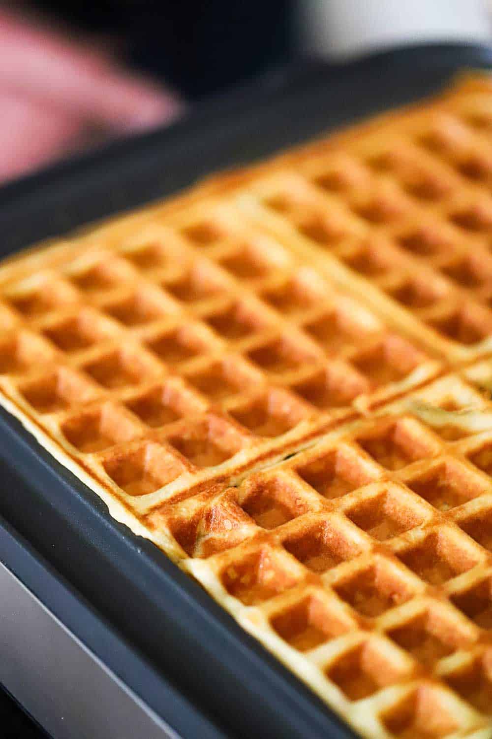 Fully cooked waffles in a square waffle maker with the lid up exposing the waffles. 