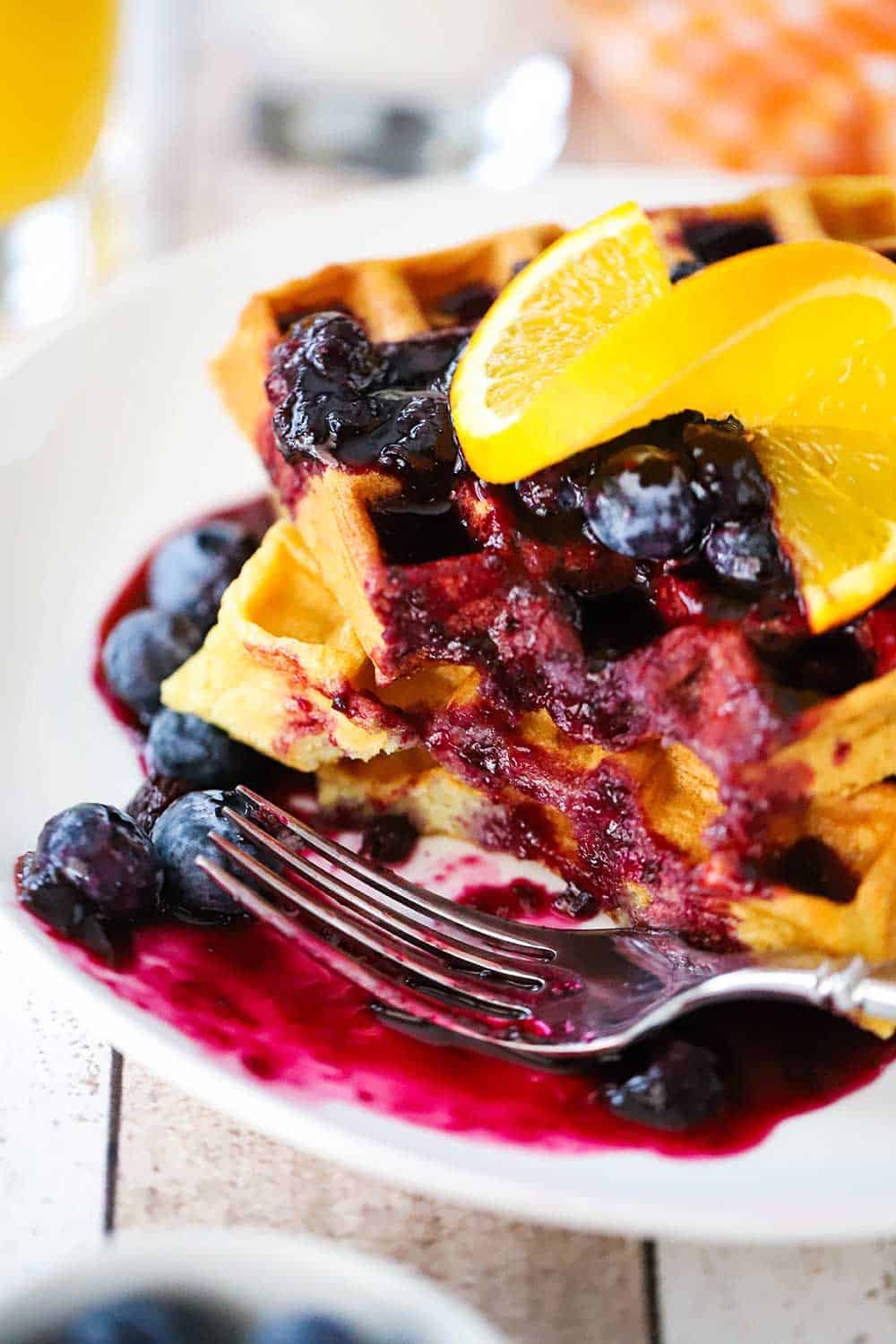 A white plate filled with a stack of buttermilk waffles and blueberry sauce with a bite take out of it. 