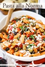 A large white oval serving platter filled with a tomato pasta topped with cooked eggplant pieces and crumbled cheese.