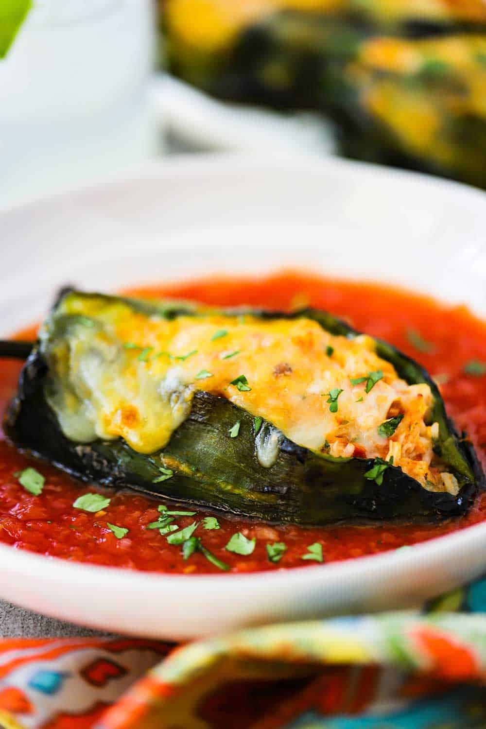 A stuffed poblano pepper on a white plate filled with a red sauce.