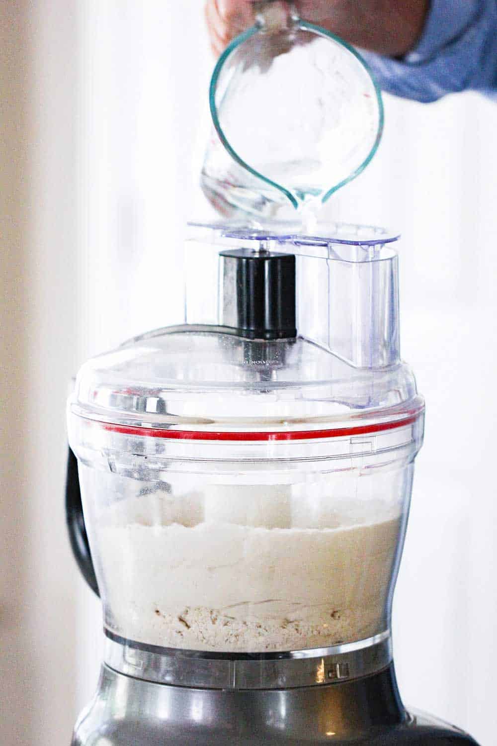 Hot water being poured into a large food processor with flour tortilla ingredients. 