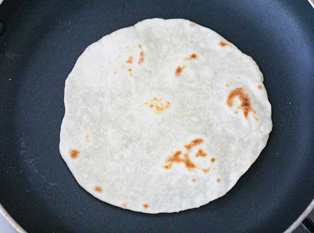 A flour tortilla cooking in a black skillet. 