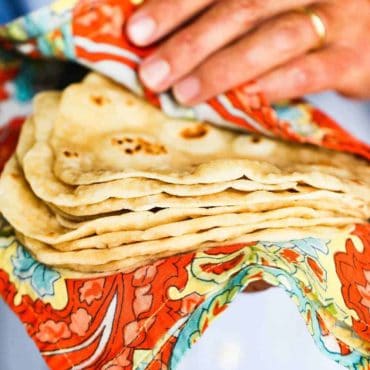 Hands holding a stack of homemade flour tortillas in a colorful cloth.