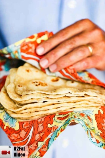A stack of homemade flour tortillas being held by two hands in a Mexican cloth.
