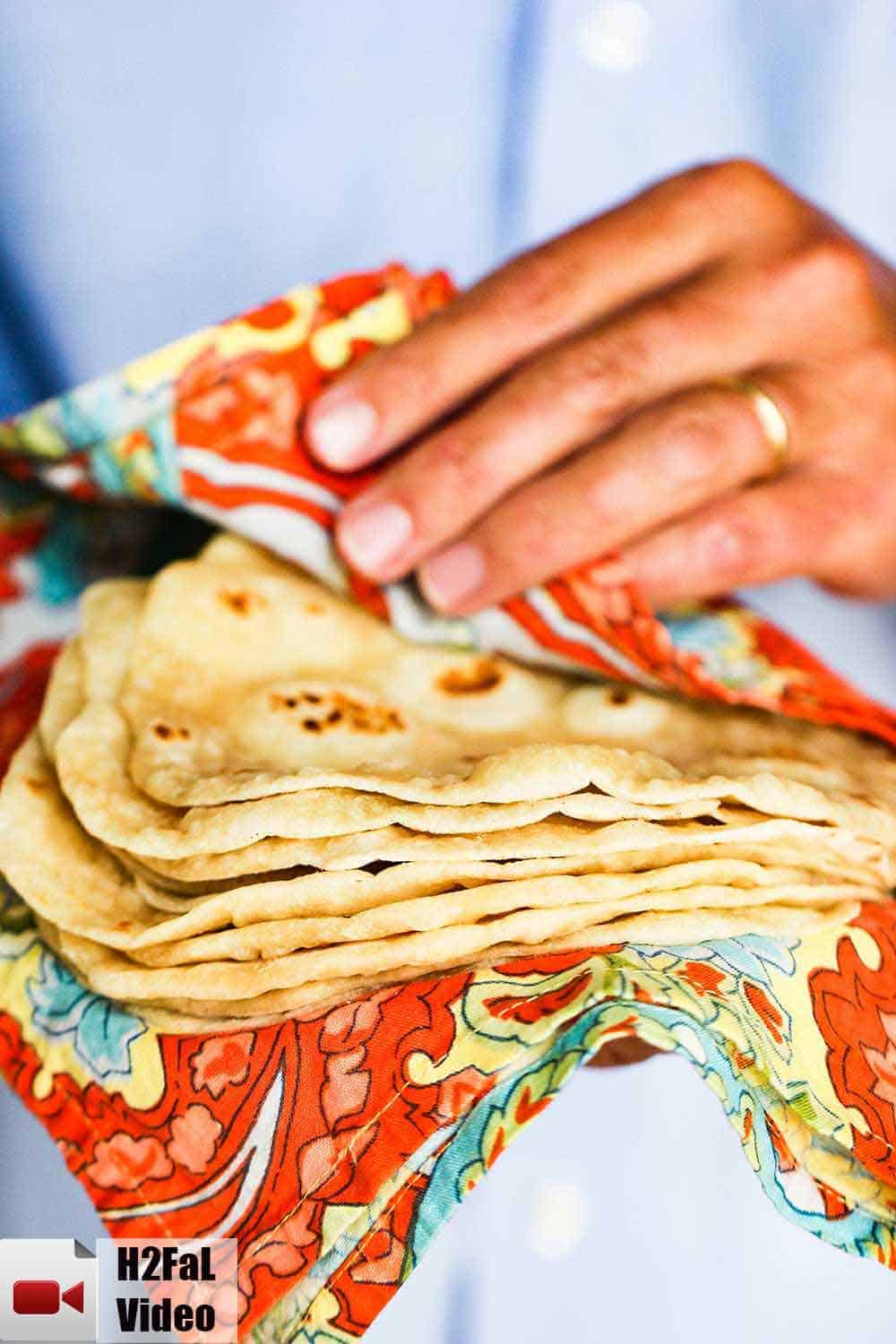 A stack of homemade flour tortillas being held by two hands in a Mexican cloth.