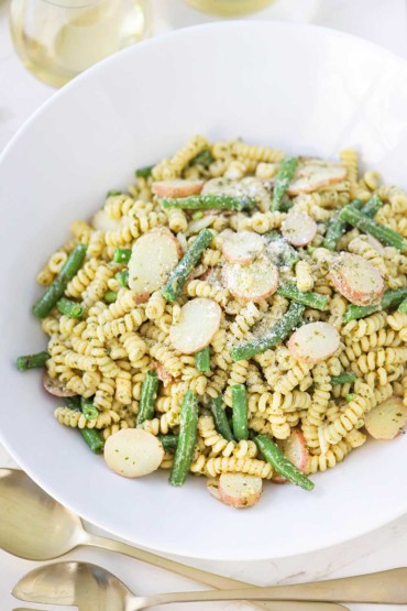 A white bowl of pesto pasta with potatoes and green beans.