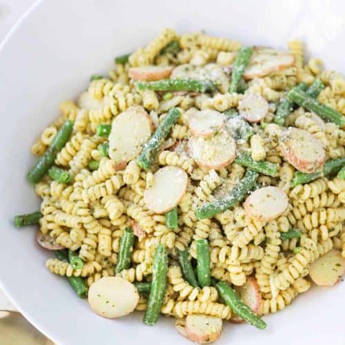 A white bowl of pesto pasta with potatoes and green beans.