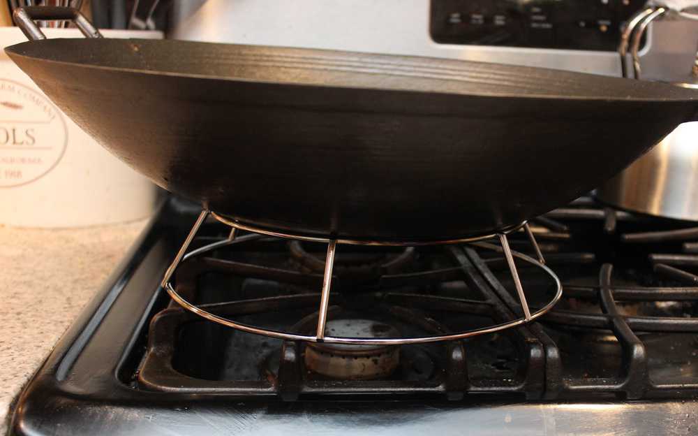 A large metal wok sitting on a wok ring on a gas stove top. 