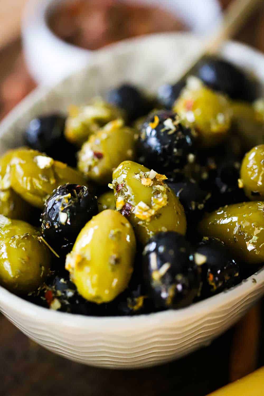 A small white oval bowl filled with green and black marinated olives. 