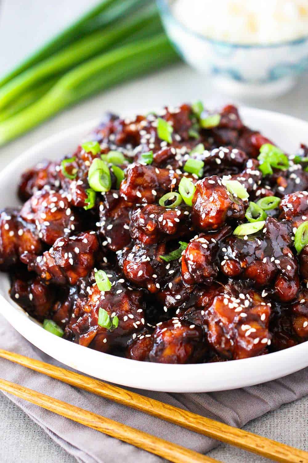 A white bowl of General Tso's Chicken with a pair of chop sticks next to it.