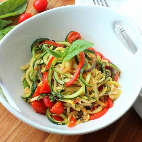 A white serving bowl filled with spiralized ratatouille next to a white napkin.