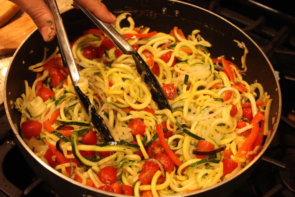A large skillet filled with spiralized ratatouille with tongs in it. 