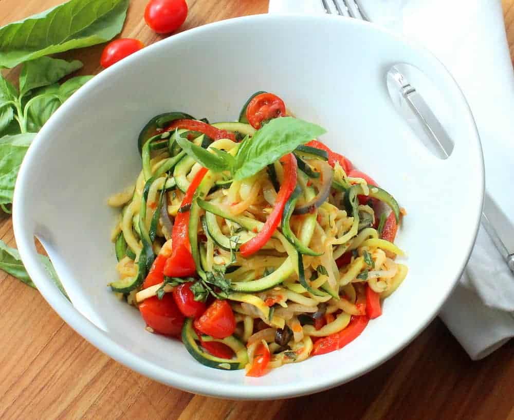 A white serving bowl filled with spiralized ratatouille next to a white napkin. 