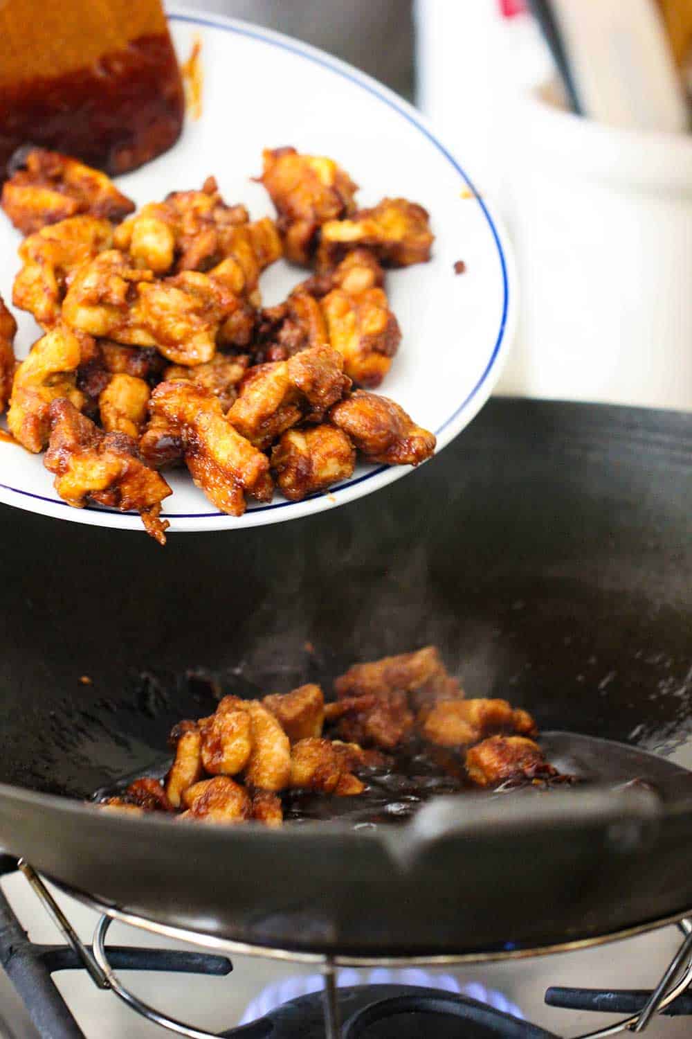 Pieces of fried chicken dropping from a platter into a wok filled with General Tso's chicken sauce. 