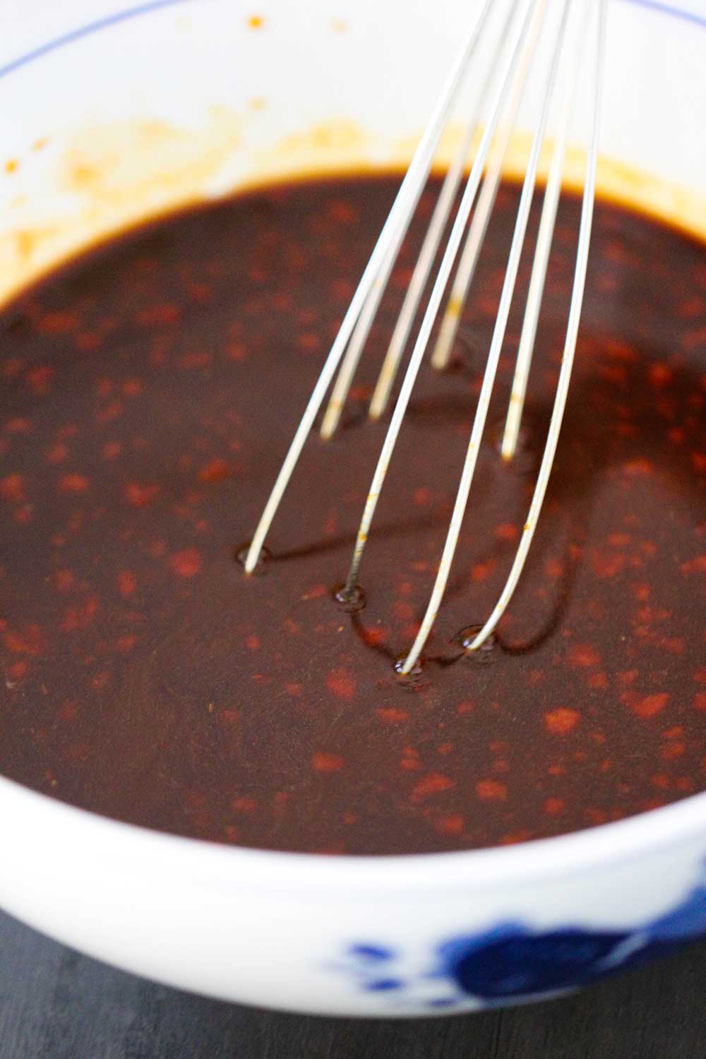 A whisk in a white bowl of General Tso's brown sauce. 