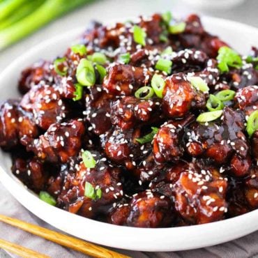 A white bowl of General Tso's Chicken with a pair of chop sticks next to it.