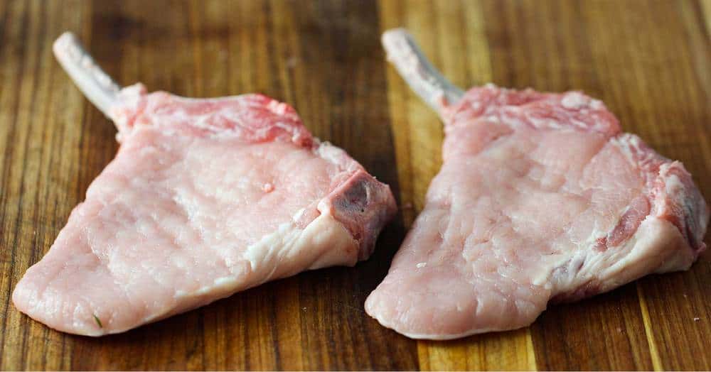 Two thin center-cut pork chops on a cutting board for Pork Milanese