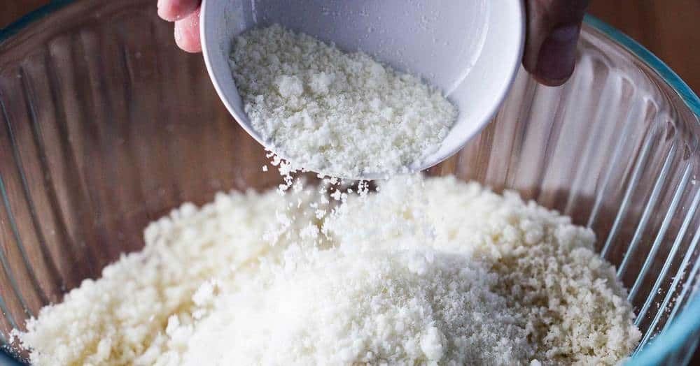 Fresh bread crumbs with Parmesan cheese being pour into a clear bowl. 