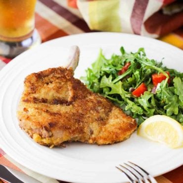 Pork Milanese on a white plate next to an arugula salad and lemon wedge.