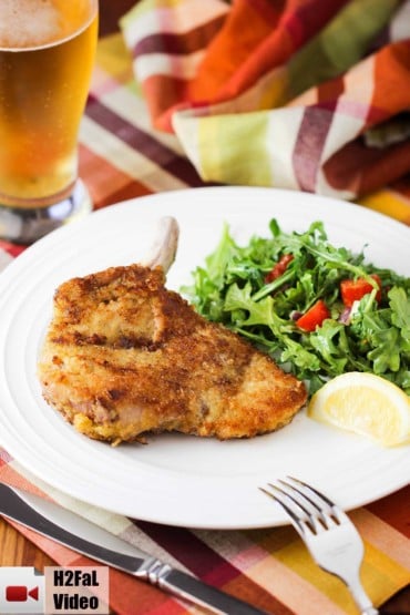 Pork Milanese with arugula salad on a white plate with glass of beer nearby.