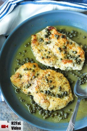 A large green skillet filled with chicken piccata and striped napkin nearby.