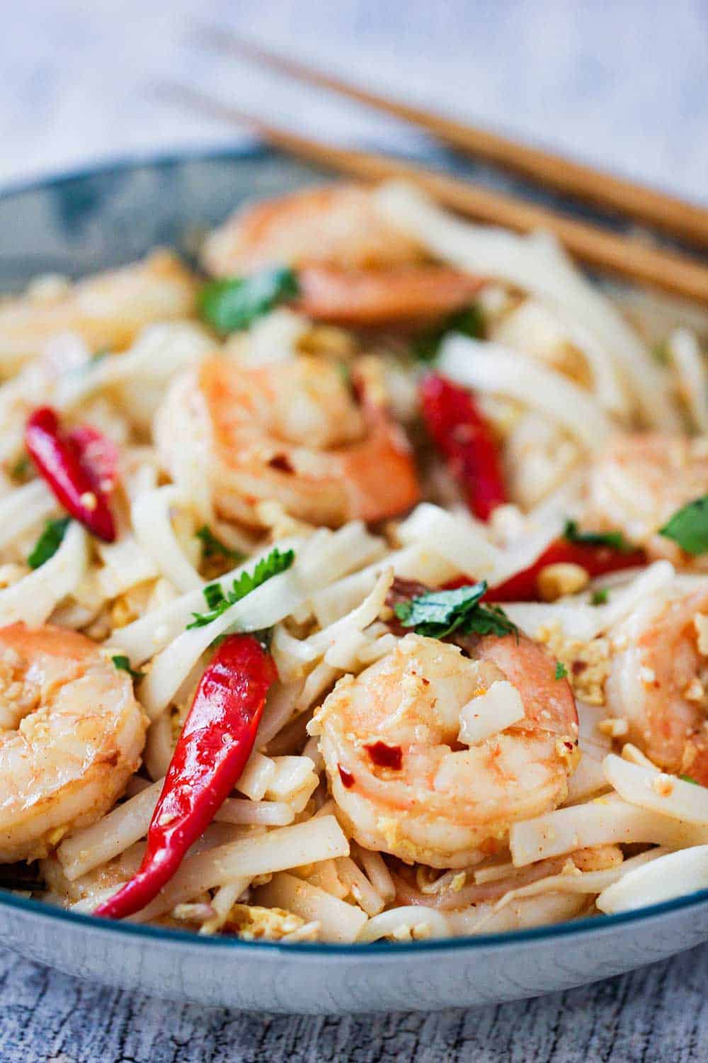 A close up view of a bowl of authentic shrimp pad Thai with two chops sticks on the side of the bowl. 