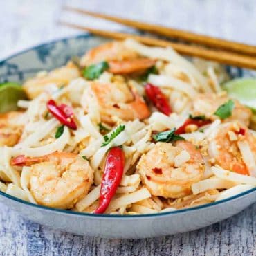 A close up view of authentic shrimp pad Thai in a colorful bowl with chop sticks next to it.