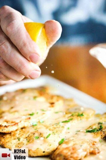 A lemon wedge being squeezed onto a platter of chicken francese