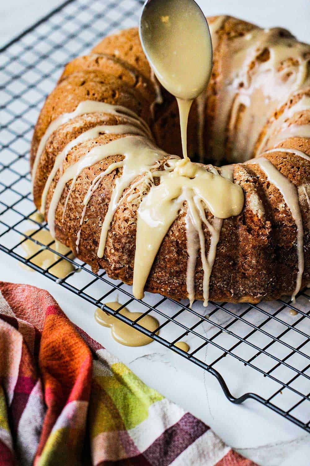 A spoon drizzling brown sugar icing over the top of a sweet potato bundt cake sitting on a wire rack. 