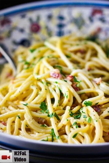A large pasta bowl layered with fresh pasta carbonara with a spoon