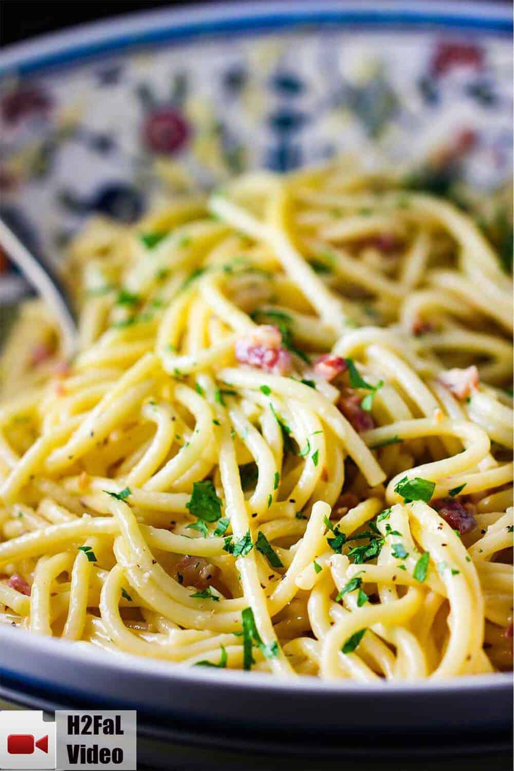 A large pasta bowl layered with fresh pasta carbonara with a spoon 