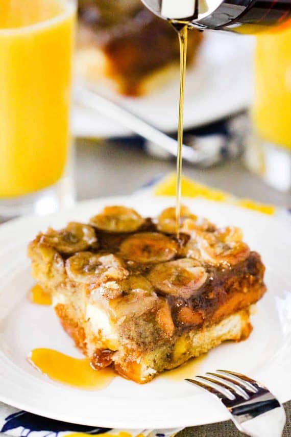 A white plate holding a piece of caramel banana baked French toast with syrup being poured over the top.