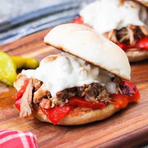 Instant Pot Italian Pulled Chicken Sandwich on a wooden cutting board with a knife and fork next to a patterned red napkin